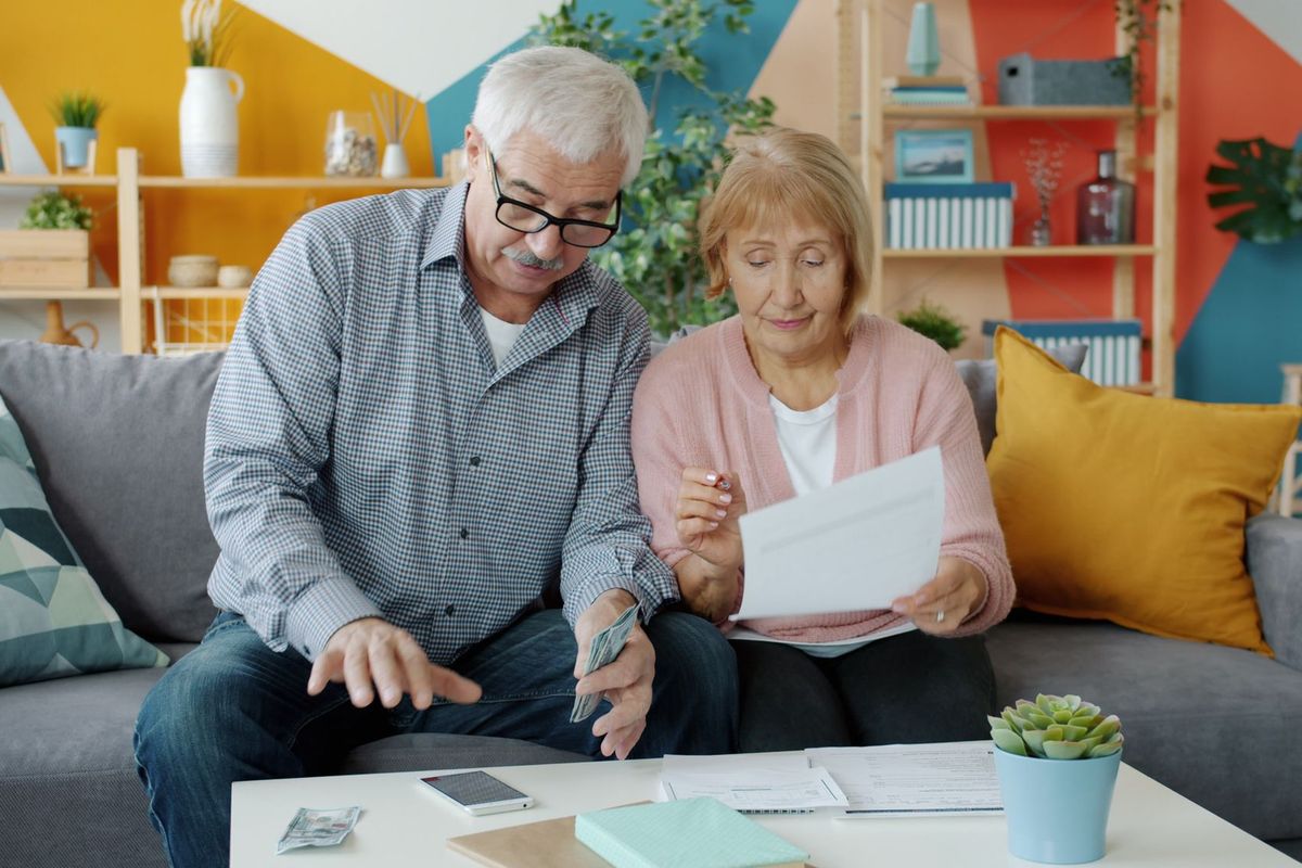 Older couple sitting on a sofa reviewing budget papers together in a colorful living room