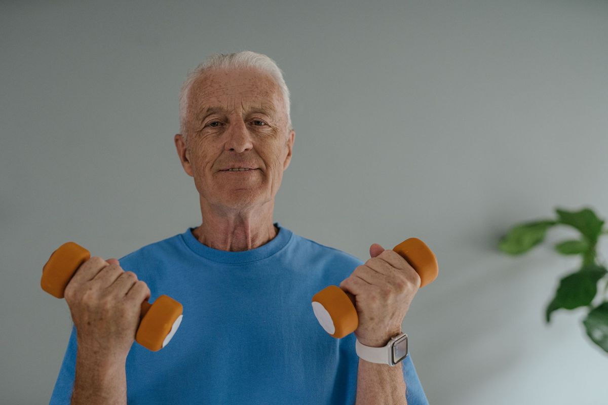 Smiling older man holding two small orange dumbbells at home